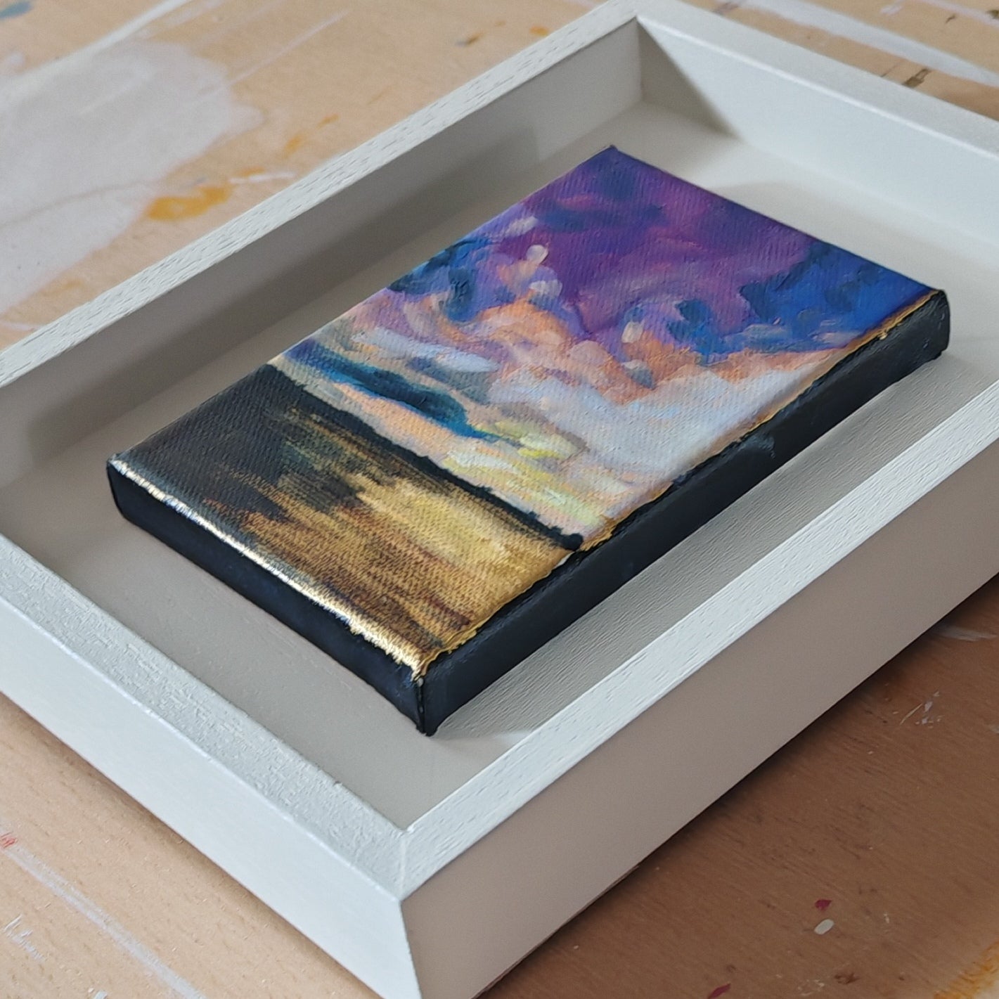 Small abstract painting on a wooden panel inside a white frame.