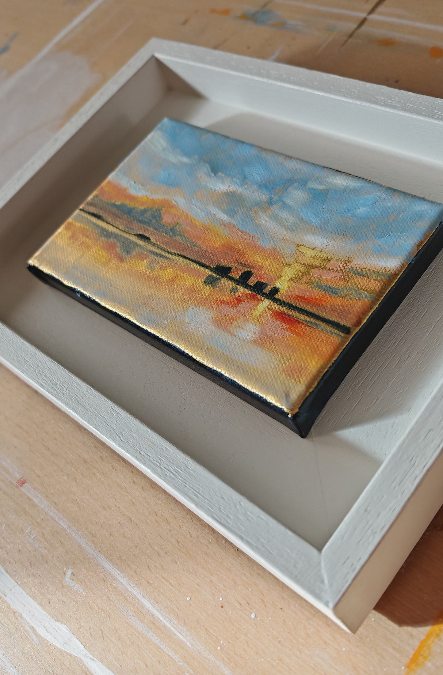 Small landscape painting in a white frame on a wooden surface