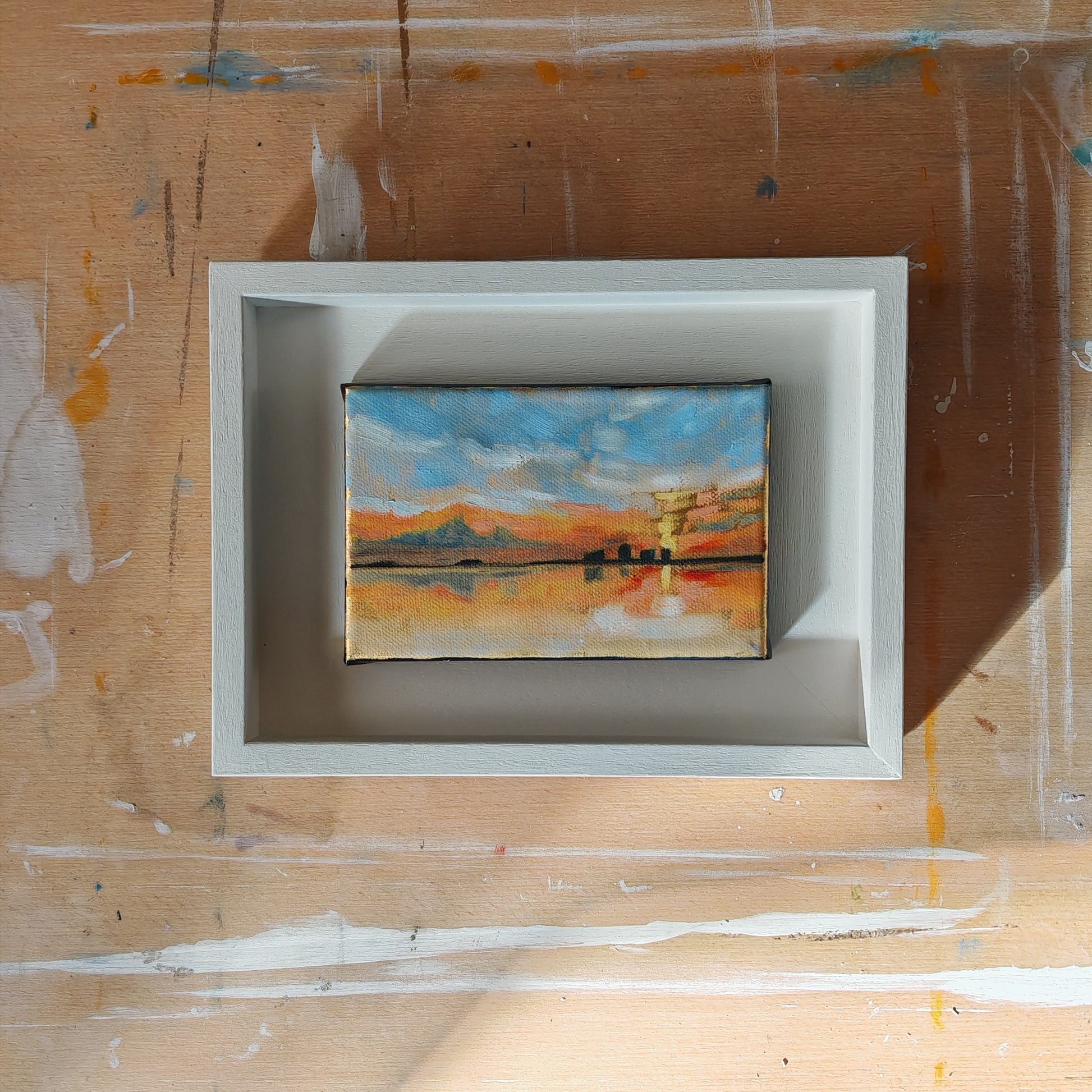 Small abstract painting inside a white frame on a wooden surface.