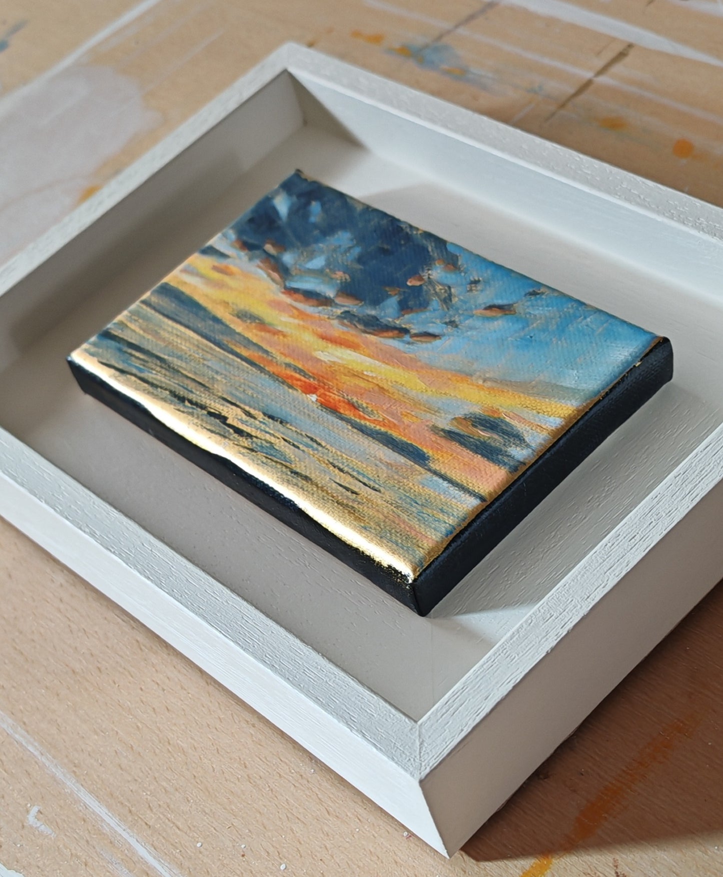 Small abstract painting in a white frame on a wooden surface